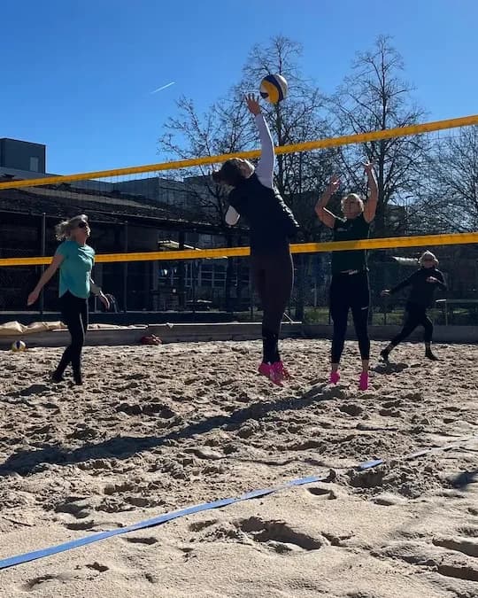 Vier Spielerinnen am Netz, eine springt zum Angriff, der Ball in der Luft